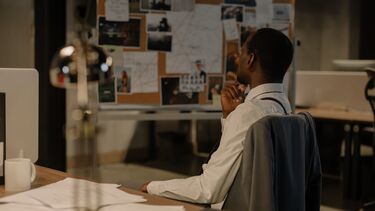 Photograph of a police detective sitting in front of a traditional crime investigation board