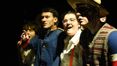 four students on a stage, one points in the distance and the other look in amazement