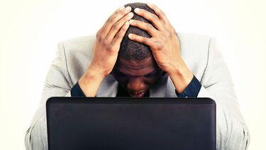 A photo of a man looking at a laptop with his head in his hands