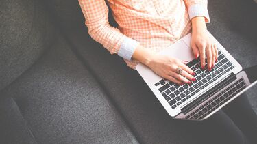 A woman sat on a sofa with a laptop on her lap.
