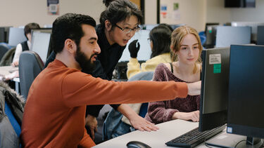  Two students looking at a computer with a lecturer