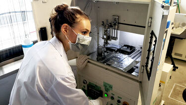 a student wearing a lab coat and goggles works conducts an experiment on a  hydrogen fuel cell