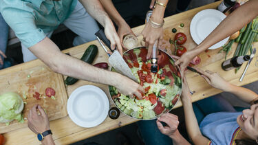 Friends preparing salad together at a dining table