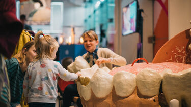 Tow adults and a small child interact with a giant sculpture of the human mouth