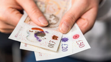 An image of a person's hands handing some cash notes towards the camera.