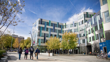 Exterior image of a grey building with coloured tiles on it, to the right of a central walkway