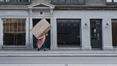 Woman walking up a street with a large box on back