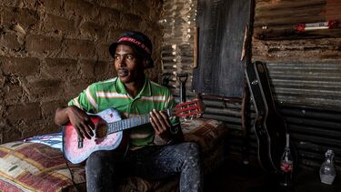 A man sitting on a bed, playing a guitar
