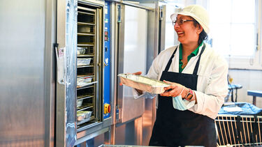 Woman in white coat and apron puts tray in oven