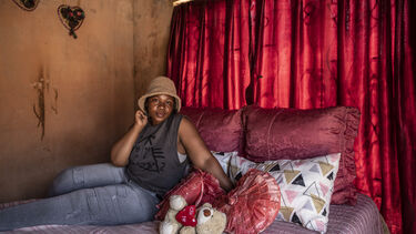 A woman wearing a hat sits on her bed