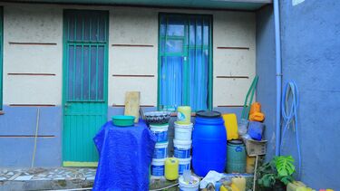 The outside of a blue and white house with tins and barrels piled up in the porch