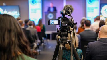 A camera filming a person speaking at a podium