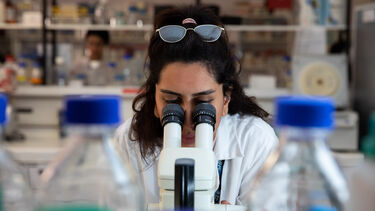 A woman looks through a microscope in a lab