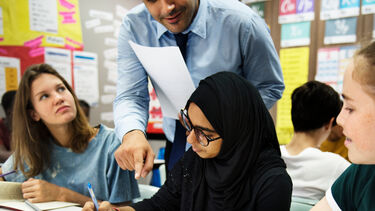 A teacher holds a sheet of paper and points to a student's book