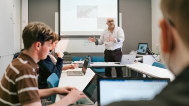 Lecturer explaining a subject to students who are using their laptops.