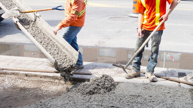 two men in hi-vis jackets shovel cement which is pouring from a tube