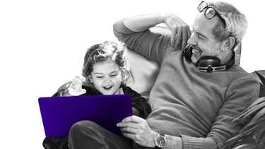 Father and young daughter sitting on sofa with a laptop