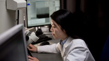 Kroto Centre PhD student at a computer and using equipment in a lab coat