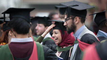Postgraduate students smiling at graduation wearing caps and robes