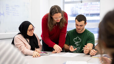 Teacher explaining something to two students in a seminar