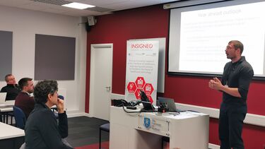 Alex Wilkinson stood in front of a project addressing Insigneo members seated at tables.