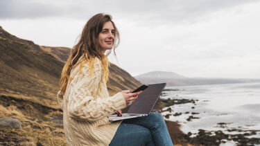 A woman using a laptop and mobile phone in a remote coastal area