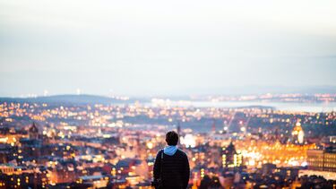 A photo of a person on a hill looking out above a cityscape lit at dusk.