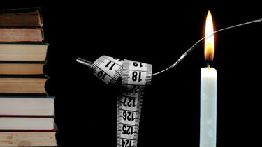 A stack of books, a fork wrapped in a tape measure and a candle.