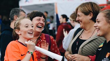 Four women and girls laughing and smiling at a women's football match