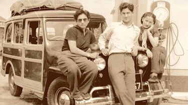 Three people sat on the bonnet of an old car