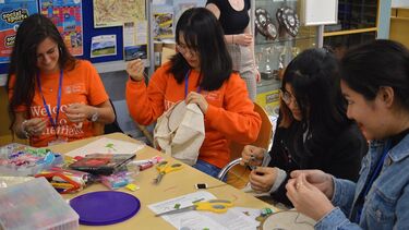 Students sit around a table working with needles, thread and various coloured fabrics
