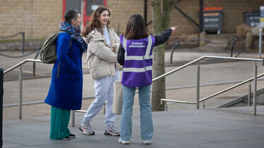 Student ambassador talking to two guests on campus at a University event.