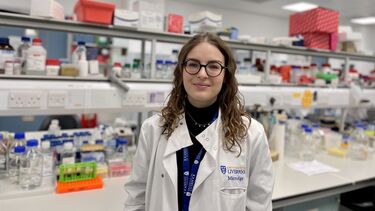 Karolina Wikaryjczyk in a lab coat, with lab equipment behind her