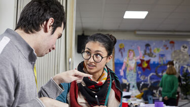 A woman speaking to a man in a classroom setting