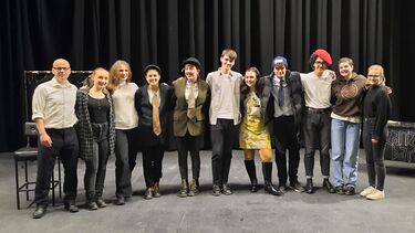 Group of 11 students and staff involved in the French play all standing arms round each other