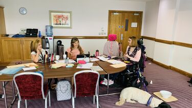 A group of three researchers sitting around a table with books, laptops and two assistance dogs.
