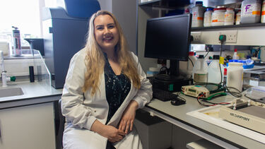 A PhD student in a lab coat in front of lab equipment