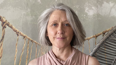 A woman with a grey bob and pink top smiles at the camera. Jungle themed wallpaper is behind her.