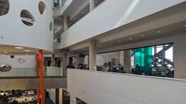 Students working at tables on lowest floor, next floor shows a walkway in front of a large computer room within a similar walkway for the floor above