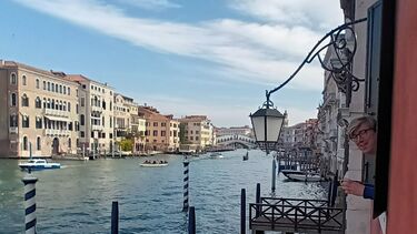 Canal in Venice with Sean Williams leaning on elbows out of a window looking at the camera