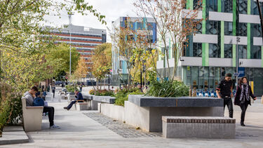 Students walking on a pedestrianised area outside of the University's Jessop West building lined with trees