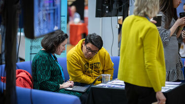 Two people sat on a sofa, looking at a laptop screen at a careers fair.