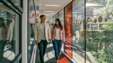 Two students walking down a corridor with glass walls.