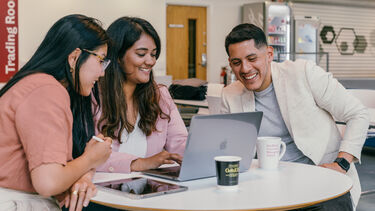 Three students working together around a laptop.