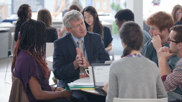 Richard Bruce in conversation with a group of students round a table.