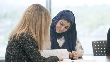 Two students sat at a desk, reading a textbook