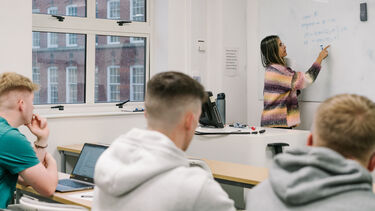 Students watching teacher explain work on a whiteboard 