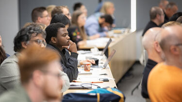 Row of people sitting in a lecture theatre listening to speakers.