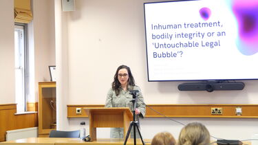 Speaker at the front of the school of law moot court with power point title slide behind delivering their presentation