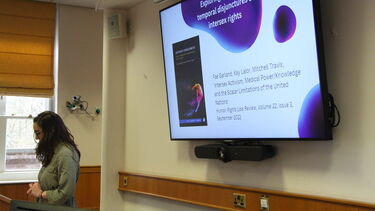 Side view of the speaker with their presentation behind them. Inside the moot court